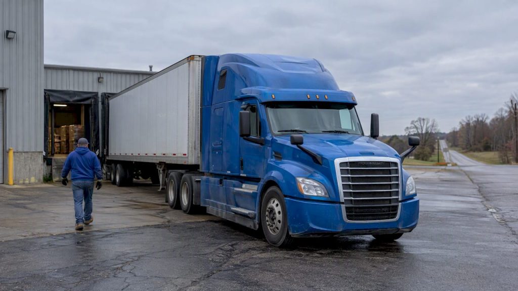 Blue tractor-trailer waiting at a rural freight yard